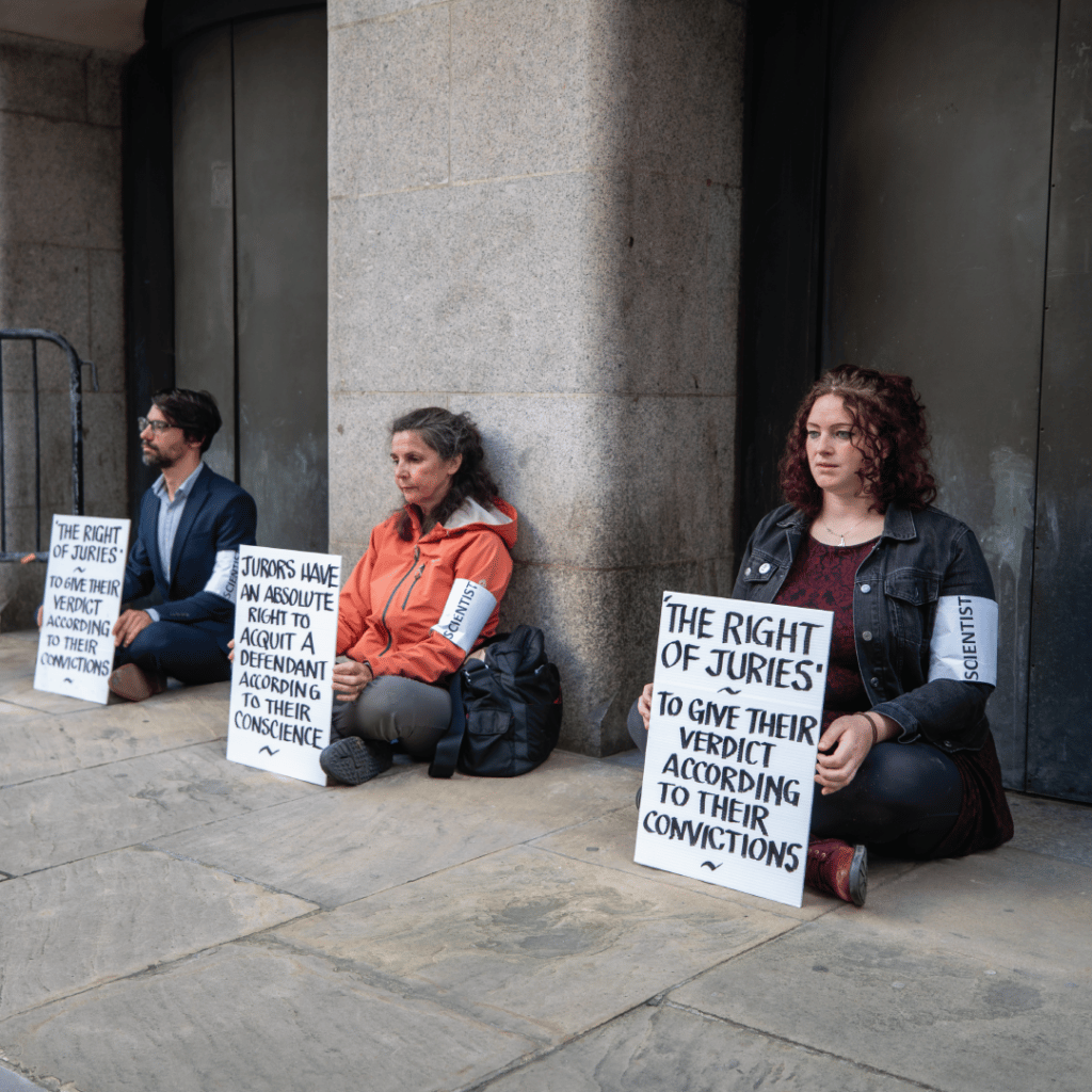 Activists sit outside a courthouse in London holding replicas of Trudi Warner’s sign in 2023.